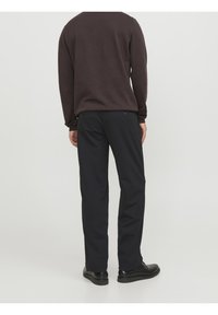 Pantalones negros de tela con una textura suave. Tienen piernas rectas y dos bolsillos traseros con cierres de botón.