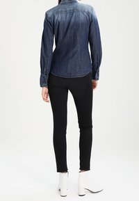 Denimskjorta i mörkblått med långa ärmar och knapparen, i kombination med svarta skinny jeans och vita ankelskor.