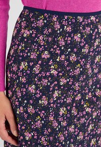 Jupe florale avec un fond marine et des motifs de fleurs roses, blanches et vertes. Taille élastique et texture de tissu lisse.