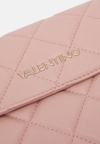 Růžová prošívaná kožená kabelka s zlatým logem "Valentino", obsahující diamantový vzor a kontrastní šití na klopě.