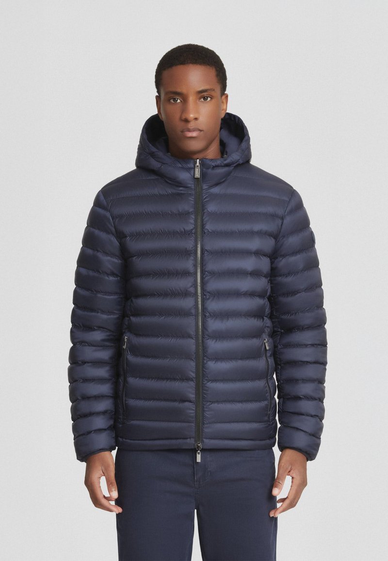 Giacca piumino navy con design trapuntato, chiusura con zip e cappuccio. Presenta tasche laterali e una texture liscia e lucida. Leggera e isolante.