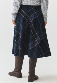 Une jupe à carreaux marine avec un design évasé, mettant en avant des lignes vertes, roses et blanches. Assortie à des bottes marron montantes. Texture douce.