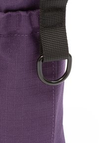 Purple fabric bag featuring a textured surface, a black strap, and a circular metal ring attachment.