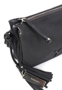 Schwarze Leder-Clutch mit durchbrochener Textur, silbernem Reißverschluss und einem Quastenakzent. Mit einem metallischen Etikett, das "SURI FREY" liest.