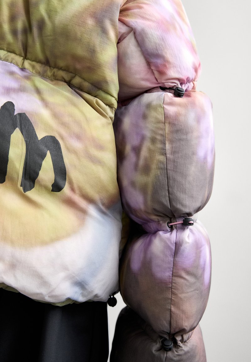 Padded bunda s vícebarevným tie-dye vzorem v pastelových odstínech, se výrazným černým logem a elastickými detaily na rukávech.