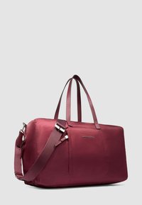 Bolsa de viaje rectangular burdeos con dos asas superiores, correa de hombro ajustable y logo "Piquadro" en la parte frontal sobre un fondo liso.