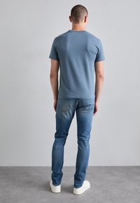 Camiseta de algodón azul claro con cuello redondo, combinada con jeans de mezclilla azul desteñida. El conjunto se complementa con zapatillas blancas.