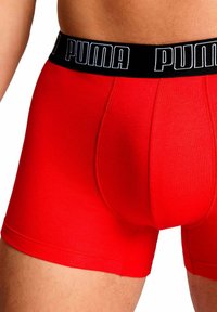 Boxer rossi con una cintura nera che presenta il logo "PUMA" in bianco. Realizzati in un tessuto liscio e elasticizzato con una vestibilità aderente.