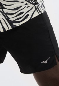 Μαύρο αθλητικό σορτς με μικρό λευκό λογότυπο στο κάτω μέρος, συνδυασμένο με λευκό και μαύρο πουκάμισο με μοτίβο.