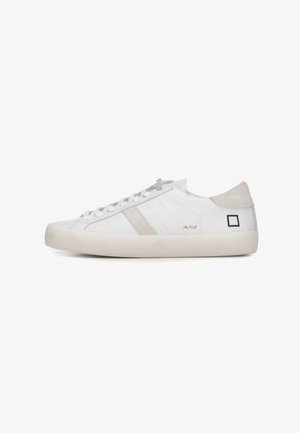 Hvid lavtop-sneaker med beige ruskindshælflig, beige sidestribe, hvide snørebånd og sort firkantet logo nær hælen på hvid sål.