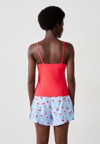 Top rosso senza maniche con design testurizzato e spalline sottili, abbinato a pantaloni corti a scacchi blu con motivo a ciliegie.