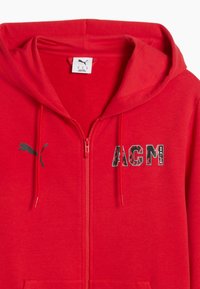 Κόκκινο φούτερ με φερμουάρ, με τσέπη καγκουρό, κορδόνια και λογότυπο. Στο μπροστινό μέρος εμφανίζεται το κείμενο «AGM» με σχεδιασμό σε μοτίβο. Μαλακή υφή ύφασματος.