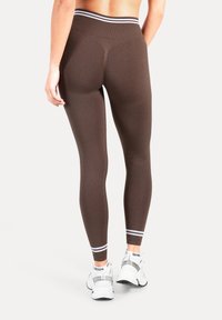 Leggings de sport marron avec une taille haute et des accents à rayures blanches à l'ourlet. Le tissu semble lisse et moulant.