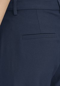 Pantalon bleu marine sur mesure en tissu lisse. Comprend une poche arrière unique avec une finition soignée, une taille structurée et une texture subtile.