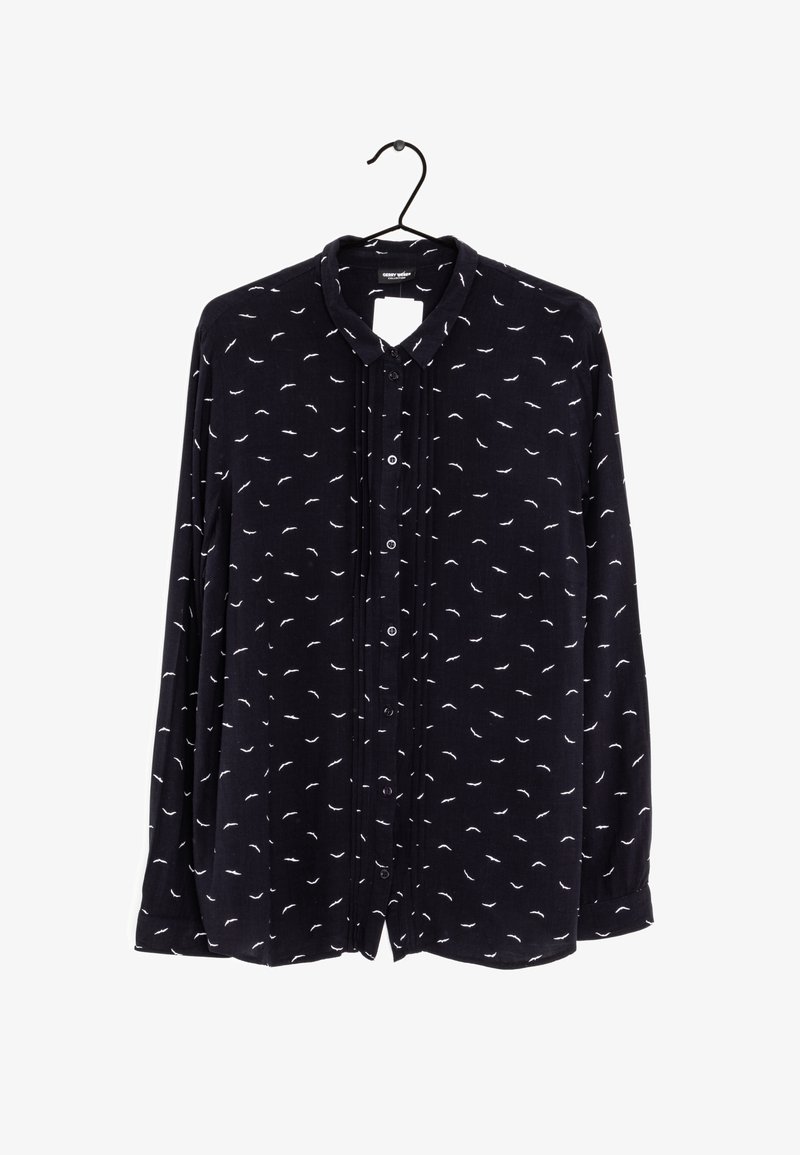 Blusa a maniche lunghe di un blu navy scuro con un piccolo motivo a piume bianche, fronte con bottoni e colletto classico. Tessuto morbido con una vestibilità leggermente ampia.