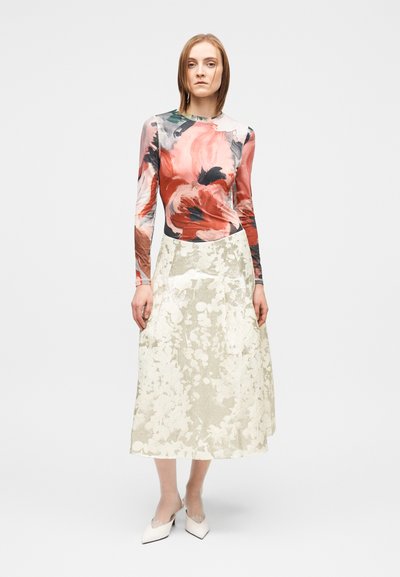 Ilgomis rankovėmis gėlėtas viršus raudonos ir juodos spalvų atspalviais, derinamas su tekstūruota, šviesios spalvos su gėlių raštu suknele. Baltos aukštakulnės batai.