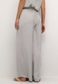 Pantalons larges gris clair en tissu fluide, dotés d'une taille élastique et de plis subtils, avec une texture douce.