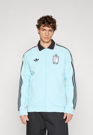 Chaqueta azul claro con cremallera, hecha de tela lisa, con cuello negro, tres rayas negras en las mangas y un logotipo bordado en el pecho.