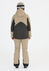 Completo da sci marrone e nero con giacca con cappuccio e pantaloni coordinati. La giacca presenta un design a blocchi di colore e un tessuto testurizzato.