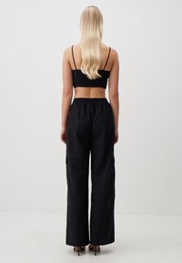 Zwarte crop top en losse zwarte broek van lichtgewicht stof, met een elastische tailleband en cargozakken.