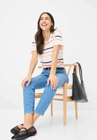 T-shirt rayé en blanc, rose et bleu marine, associé à un jean bleu clair. Des chaussures en mesh noires et un sac à main noir texturé complètent le look.