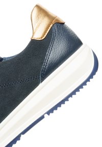 Nahaufnahme eines marineblauen Sneakers mit strukturiertem Leder und Wildleder, metallisch goldenem Fersenlaschen und dicker weißer Sohle mit blauem Profil.