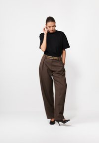 Czarny t-shirt z krótkim rękawem z wytłoczonym napisem, zestawiony z brązowymi spodniami w kratę o wysokim stanie i paskiem w panterkę. Gładkie czarne szpilki.