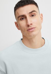 Lichtblauwe sweater met een ronde halslijn en geribbelde boorden. Zachte stoftextuur met een relaxte pasvorm. Gemaakt met een gefocuste blik op het bovenlichaam van het model.