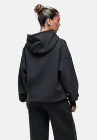 Felpa nera oversize con cappuccio, dal tessuto morbido, caratterizzata da una vestibilità rilassata e maniche ampie. Dettagli di cucitura visibili sul retro.