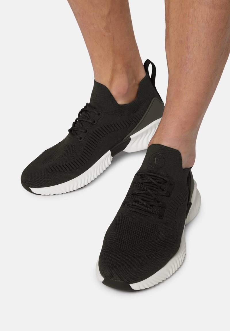 Svarta sportskor med en stickad ovandel, som har snörning, en dragflik och en kontrasterande vit sula med texturerade inslag.