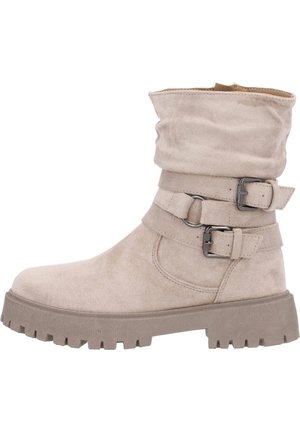 Beige Knöchelstiefel mit einem fallenden Schaft, zwei verstellbaren Riemen mit silbernen Schnallen und einer dicken, strukturierten Sohle. Hergestellt aus weichem, wildlederähnlichem Material.
