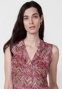 Canottiera senza maniche con motivo a zigzag che presenta tonalità di rosa, rosso e oro. Chiusura con bottoni frontale, due tasche sul petto e vestibilità rilassata.
