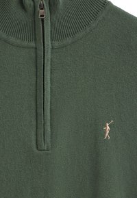 Grön zip-up tröja med hög krage, ribbat mönster och en liten beige golfer-logga på vänster bröst. Tillverkad av mjukt stickat material.