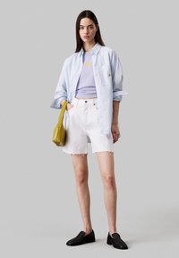 Camisa de botón a rayas azul, top sin mangas lavanda, pantalones cortos de mezclilla blanca con dobladillo deshilachado, bolso amarillo, zapatos negros sin cordones.