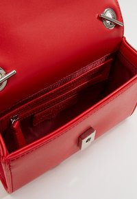 Borsa a tracolla rossa in pelle con chiusura a scatto magnetico, accessori in argento e interno foderato con più scomparti e etichetta con logo.