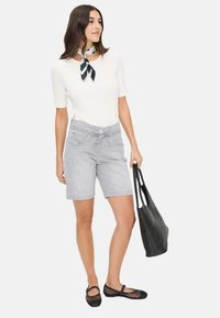 Grijze denim shorts met een trekkoord in de taille, gecombineerd met een witte, aansluitende top en een zwart-wit patroon sjaal, terwijl ze een zwarte tote bag vasthoudt.