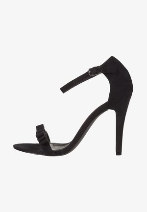 Black suede high-heeled sandal featuring a thin ankle strap, a ruffled front strap, and a sleek stiletto heel, offering a minimalist design.