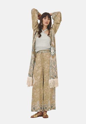 Kimono ligero y estampado con mangas de flecos, combinado con una blusa gris y pantalones beige de pierna ancha con cintura ajustable. Sandalias doradas.