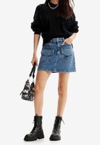 Džínová mini sukně se dvěma předními kapsami a dekorativním prošíváním; doplněná o černý texturovaný svetr a černé šněrovací vojenské boty.