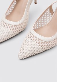 Zapatos de tacón alto con cordones en beige, con punta afilada, diseño de malla abierta y ribete de cuero suave con un delgado tacón de aguja.