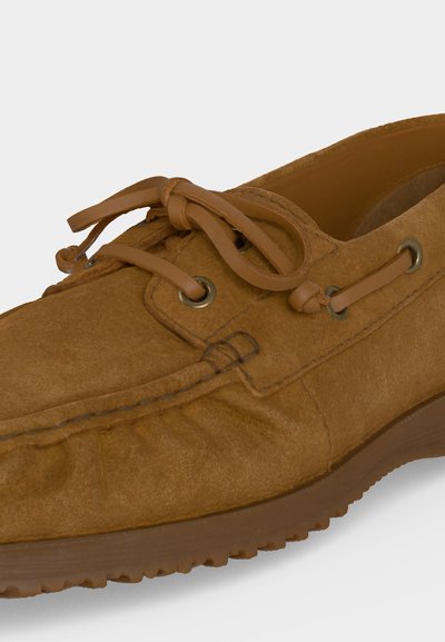 Chaussure mocassin en daim marron avec un lacet en cuir noué en nœud et une semelle en caoutchouc.