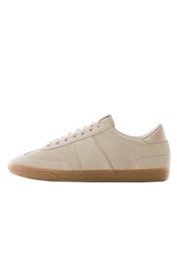 Beige tenisky s hladkým semišovým svrškem, gumovou špičkou a gumovou podrážkou. Vybavené plochými tkaničkami a jemnými švy.