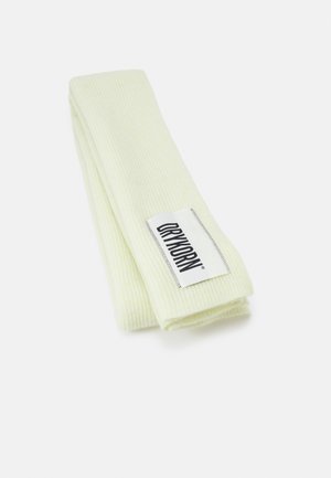 Foldet lysegul ribstrikket tørklæde med en hvid etiket syet nær kanten med teksten "DRYKORN" i sorte bogstaver.