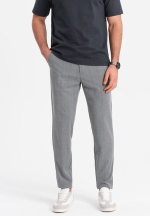 Pantalons gris à carreaux avec une coupe ajustée, présentant une texture lisse et un pli sur le devant. Associés à des baskets blanches.