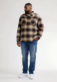 Beige, laivastonsininen ja keltainen ruudullinen flanellipaita; kaksi nappitolppaista etutaskua; yhdistetty sinisiin farkkuihin ja valkoisiin lenkkareihin.