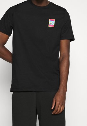 Czarna koszulka z małą kolorową grafiką gór oraz logo "adidas" w górnej lewej części, noszona z dopasowanymi czarnymi spodniami.