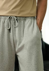 Person wearing light gray sweatpants with a drawstring and a beige shirt, hand resting in the right pocket.