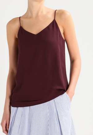 Camisole en soie bourgogne avec fines bretelles, dotée d'un décolleté en V et d'une coupe ample, associée à une jupe rayée bleu clair et blanche.