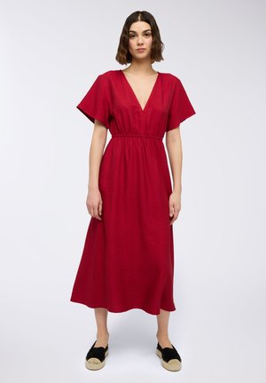 Abito midi rosso con scollatura a V profonda, maniche corte e larghe, e vita elastica. Tessuto liscio e silhouette fluida. Abbinato a espadrillas nere.