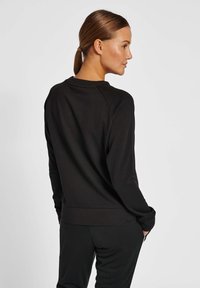 Svart sweatshirt med rund halsringning, raglanärmar och slimmad midja. Tillverkad av ett mjukt, strukturerat tyg med en slät yta.